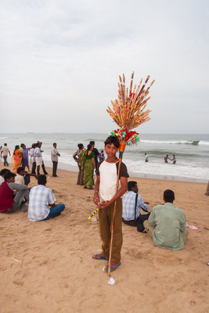 Chennai, India - September 6, 2007: A local boy selling toys and souvenirs poses for a photo at Marina Beach in Chennai as other people enjoy themselves in the background.のeditorial素材