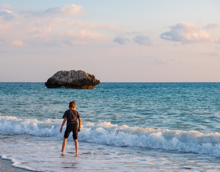 A barefooted boy plays at the beach at the Petra tou Romiou rocks, in Paphos, Cyprus. The beach is considered to be Aphrodite's birthplace in Greek mythology.の写真素材
