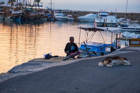 Kyrenia, Cyprus - November 27, 2018: An african man is looking at a dog sleeping on the tarmac at the old harbor of Kyrenia in Cyprus on a beautiful afternoonのeditorial素材