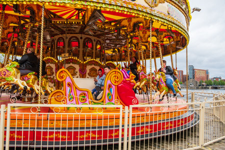 Liverpool, United Kingdom - April 26, 2019: People enjoy themselves on a carousel at the Liverpool Docks, Port of Liverpool, late on a cloudy afternoonのeditorial素材