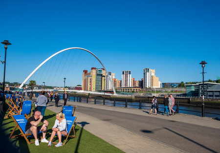 Newcastle, United Kingdom -June 27, 2019: Scene set against the Gateshead Millennium Bridge and the Baltic Centre for Contemporary Art of people enjoying themselves at the Newcastle Quayside on a beautiful summer afternoon.のeditorial素材