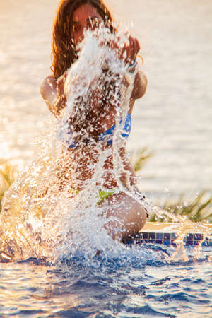 A young woman plays at the pool by the sea splashing water in Pomos, Cyprusの写真素材