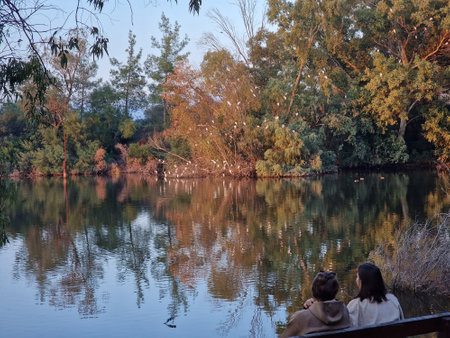 Two girls rest on a wooden bench and enjoy the lake view at Athalassa National Park in Nicosia, Cyprusの写真素材
