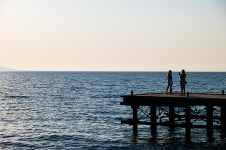 Silhouettes of a wman taking the photo of another woman on a derelict pier in Argaka in Cyprus.