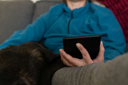 Woman reading on an electronic reading device while petting her dogのeditorial素材