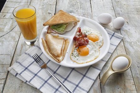 Breakfast of scrambled eggs with bacon, pancakes, sandwich and orange juice. on a wooden tableの写真素材