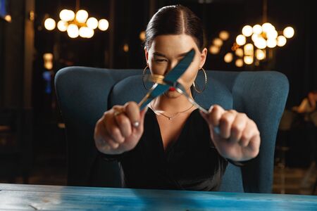A hungry girl is waiting for food. Holding a knife and fork