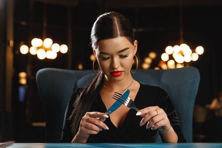 A hungry girl is waiting for food. Holding a knife and fork
