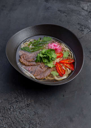 Traditional vietnamese pho bo soup in dark plate. Selective focus