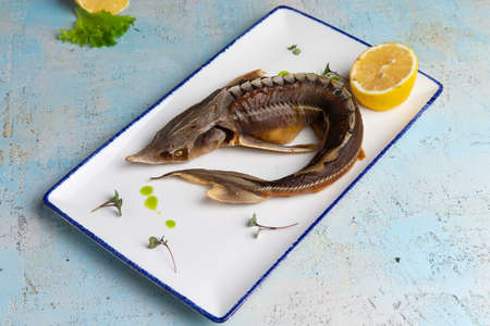 smoked fish sturgeon in a plate with lemon on a gray background