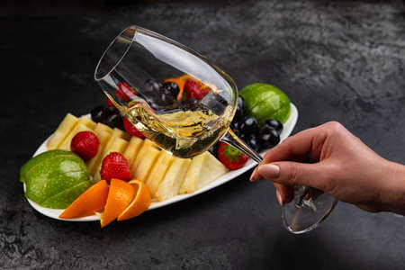 Hand holds a glass of white wine. Against the background of berries. Selective focusの写真素材