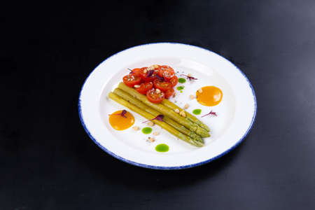 Fried asparagus and tomatoes in a plate on a dark background. Vegetarian foodの写真素材