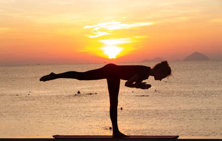 Silhouette of a young woman doing yoga near the sea at sunset. Harmony, meditation and healthy lifestyle conceptの写真素材
