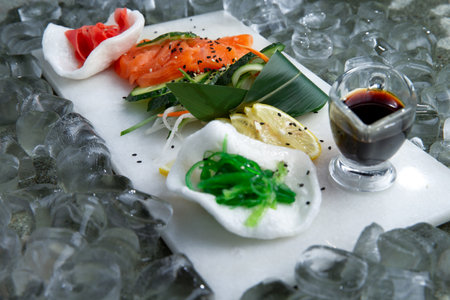 Salmon sashimi with vegetables and soy sauce on a light plate.の写真素材