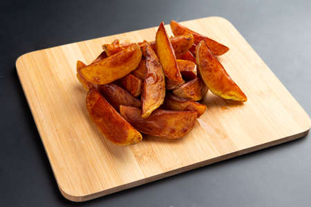Potato wedges on a board. On a dark background