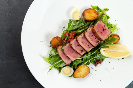 fried tuna on a pad of green beans and young potatoes on a plate.