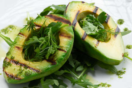 Fried avocado and greens in a plate on a gray background. Selective focus.