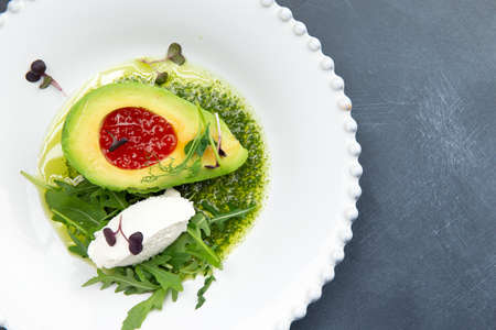 Snack. Avocado with red caviar and arugula in a plate. On a gray background. Selective focus.の写真素材