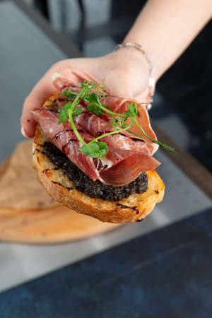 Hand holds bruschetta with ham. Against a dark background. Selective focus.の写真素材