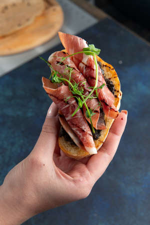 Hand holds bruschetta with ham. Against a dark background. Selective focus.の写真素材