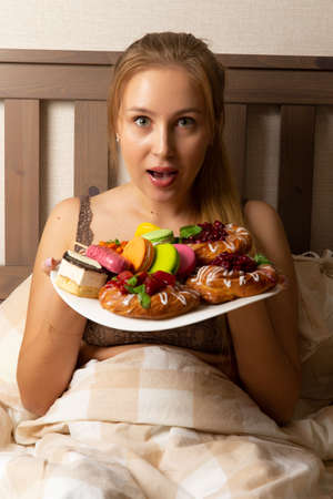 Girl in bed with a plate full of sweets. Selective focus.
