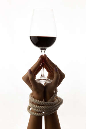Tied female hands hold a glass with alcohol isolated on a white background.の写真素材