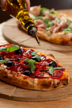 Pour olive oil on a Roman pizza with pepperoni and olives. Selective focus.の写真素材