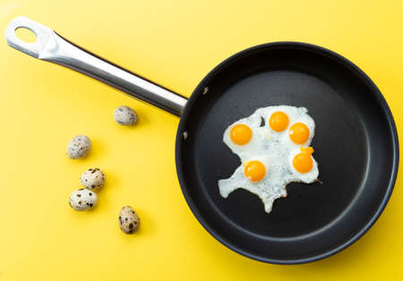 Fried eggs from quail eggs in a skillet. on a yellow background. Selective focus.の写真素材