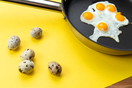 Fried eggs from quail eggs in a skillet. on a yellow background. Selective focus.の写真素材