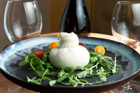 Burata cheese in a plate. Against the background of a bottle of wine and glasses. Selective focus.