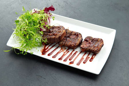 Fried tongue and greens in a plate. On a gray background. selective focus.