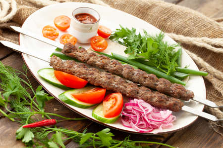 Kebab on a skewer and vegetables in a plate. On a wooden table.の写真素材