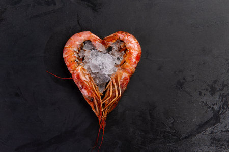 Large cooked shrimp lie in the shape of a heart on a dark background.の写真素材