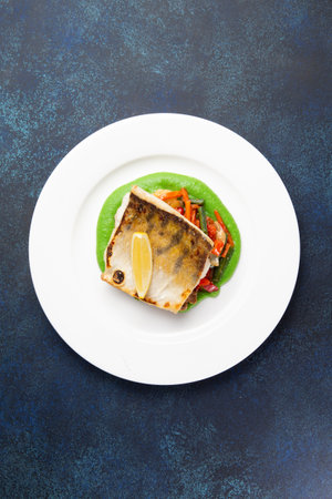 Cod steak on a bed of vegetables in a plate on a dark background.の写真素材