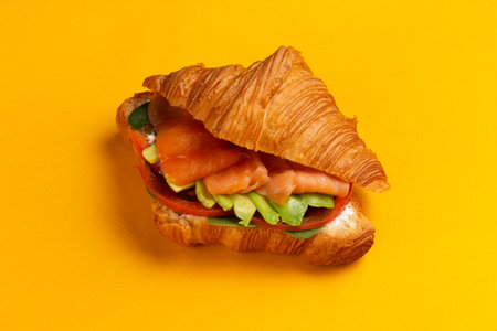 Croissant with salmon and avocado on a yellow background. Selective focus.の写真素材