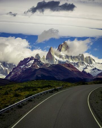 Asphalted road with the peaks of a rocky and snowy mountain on the horizon. Fitz Roy mountain in Argentinaの写真素材