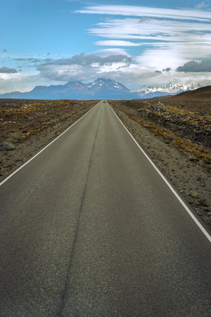 Asphalted road with the peaks of a rocky and snowy mountain on the horizon. Fitz Roy mountain in Argentinaの写真素材