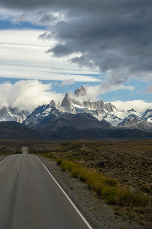 Asphalted road with the peaks of a rocky and snowy mountain on the horizon. Fitz Roy mountain in Argentina vertical Photographの写真素材
