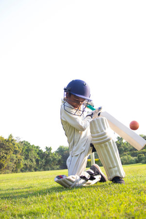 Young boy batting in protective gear during a cricket