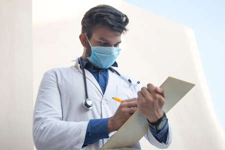 A health worker in Lab Coat Writing a notepad and penの写真素材