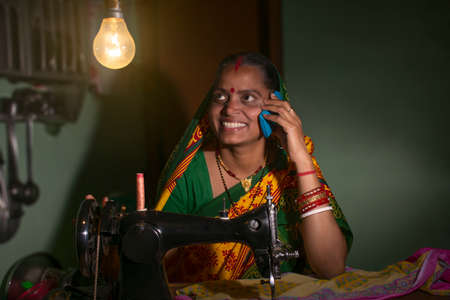 Indian rural woman using sewing machine and talking on a mobile phone