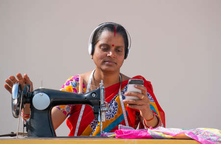 PORTRAIT OF A RURAL WOMAN listening music AND SEWING CLOTHES holding mobileの写真素材