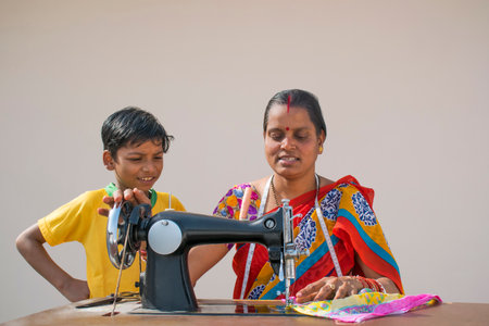 PORTRAIT OF A RURAL WOMAN STITCHING CLOTHS WITH SON BEHIND STANDINGの写真素材