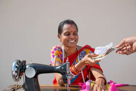 PORTRAIT OF A RURAL WOMAN using sewing machine and received counting moneyの写真素材