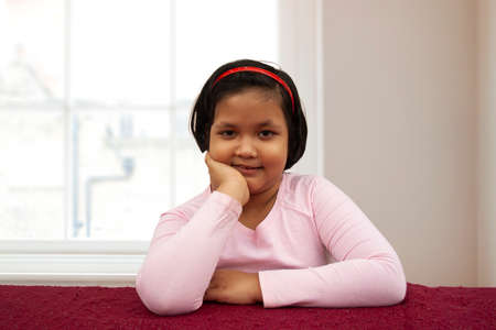 Portrait of smiling girl with hand on chin while sitting at desk in homeの写真素材