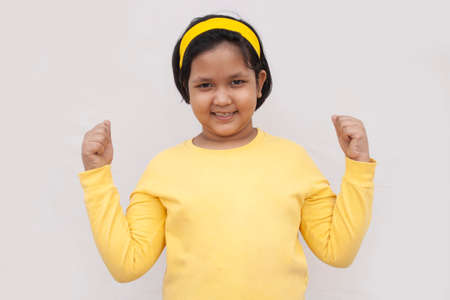 Portrait Of Smiling Girl Flexing Muscles Against grey Backgroundの写真素材