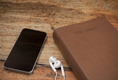 Physical Bible and a Smart Phone with Earphones on a Wood Tableの写真素材