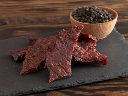 A Pile of Black Pepper Beef Jerky on a Rustic Wooden Tableの写真素材