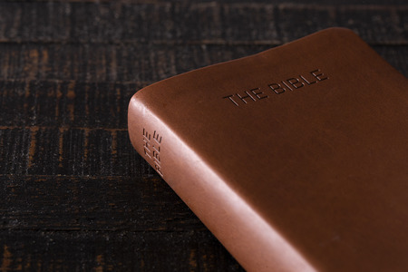 A Bible on a Wooden Table in a Dark Environmentの写真素材
