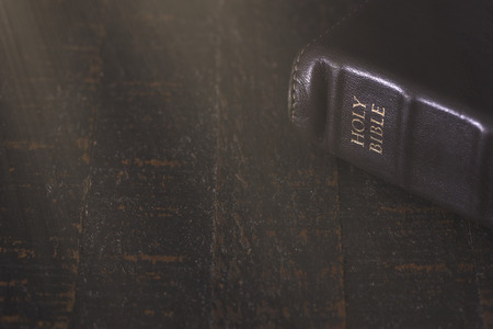 A Bible on a Wooden Table in a Dark Environmentの写真素材